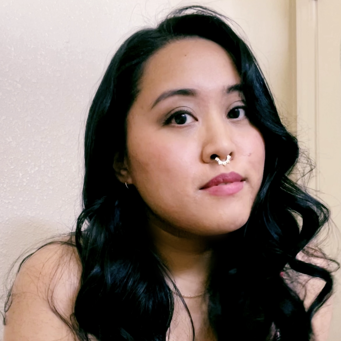 portrait of filipino woman with black hair with a gold septum piercing looking straight into the camera