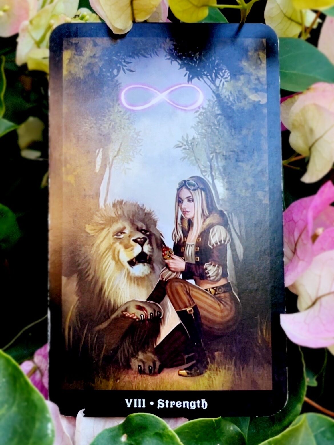 Tarot card illustrating a lion with a wounded paw and a woman helping them remove the injurious object. A purple glowing lemniscate floats above them. Below the image is the title of the card: "VIII - Strength"